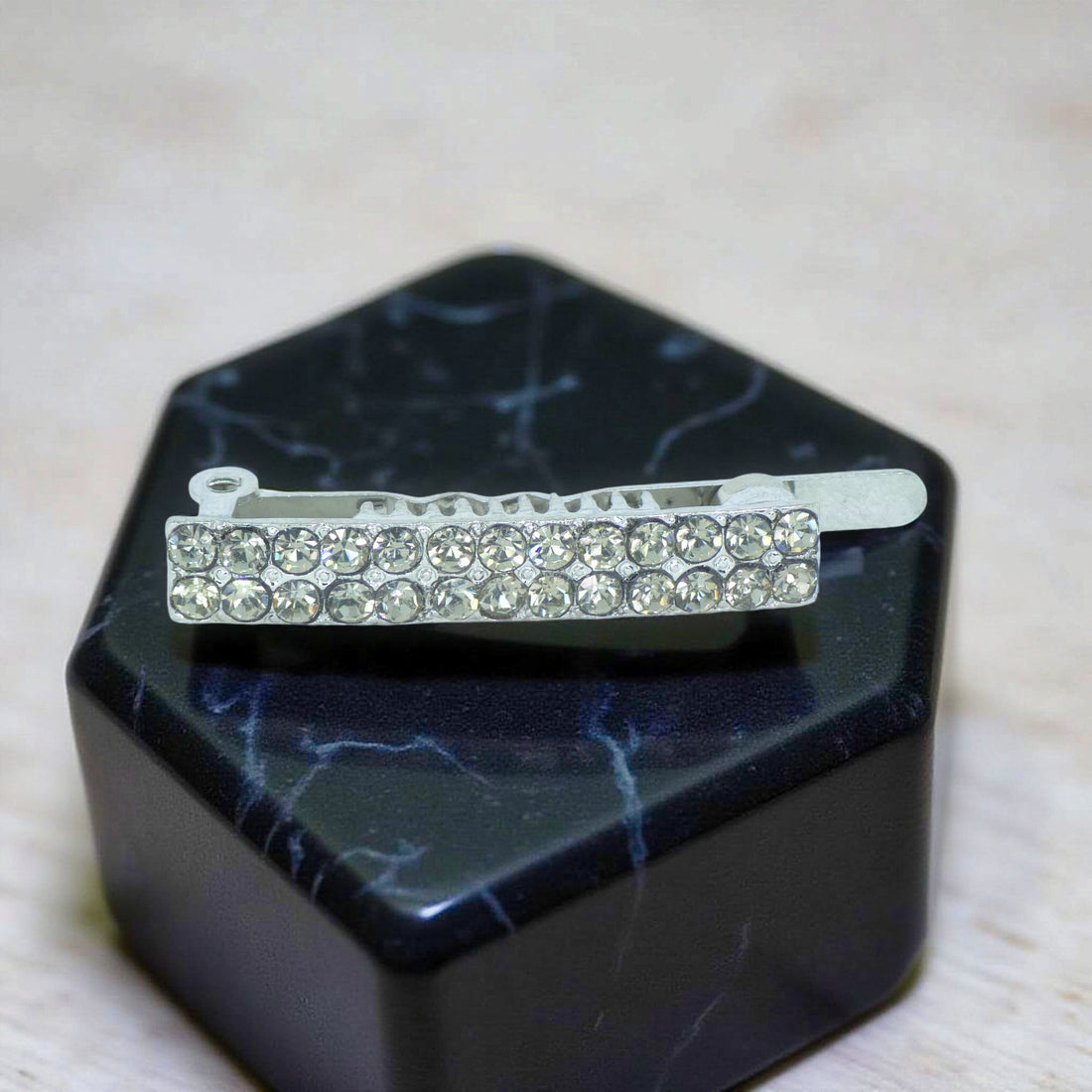 Haerime Minette Magnet Clip in Jet Black – top view showing glossy black crystal bar with curved edge on beige satin