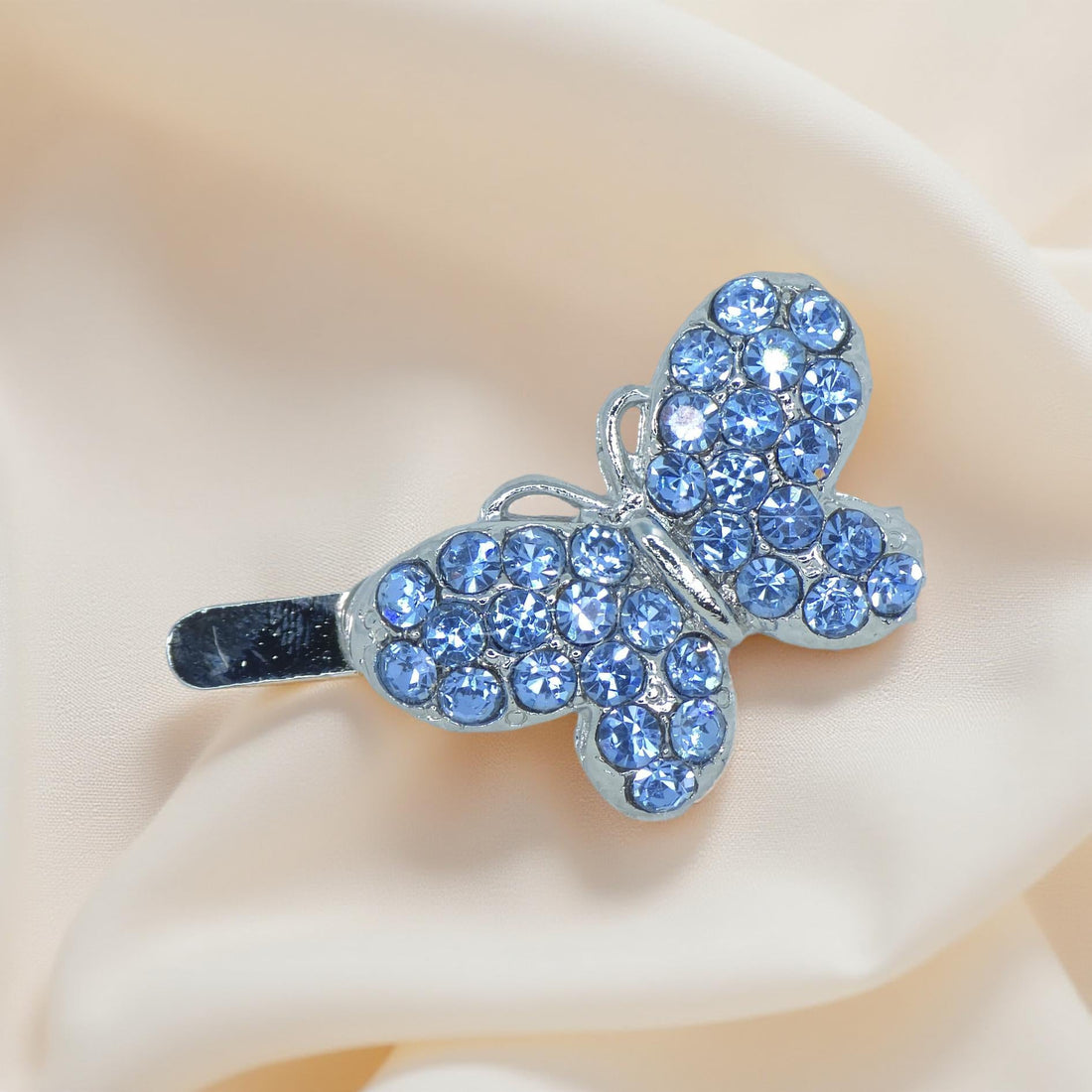 Haerime Papillon Éclat Clip in Blue – top-down view of sapphire crystal butterfly on pale satin pouch
