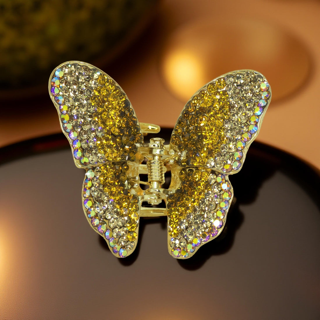 Haerime Papillora Mini Claw in Amber – close-up of honey-hued pavé wings and magnetic jaw curve over soft beige pouch
