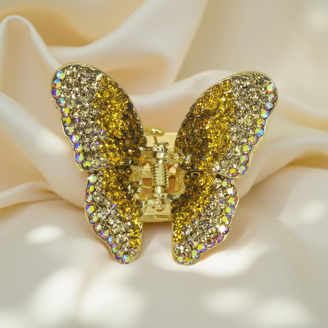Haerime Papillora Mini Claw in Amber – top-down image of golden crystal butterfly clip on light peach satin fabric