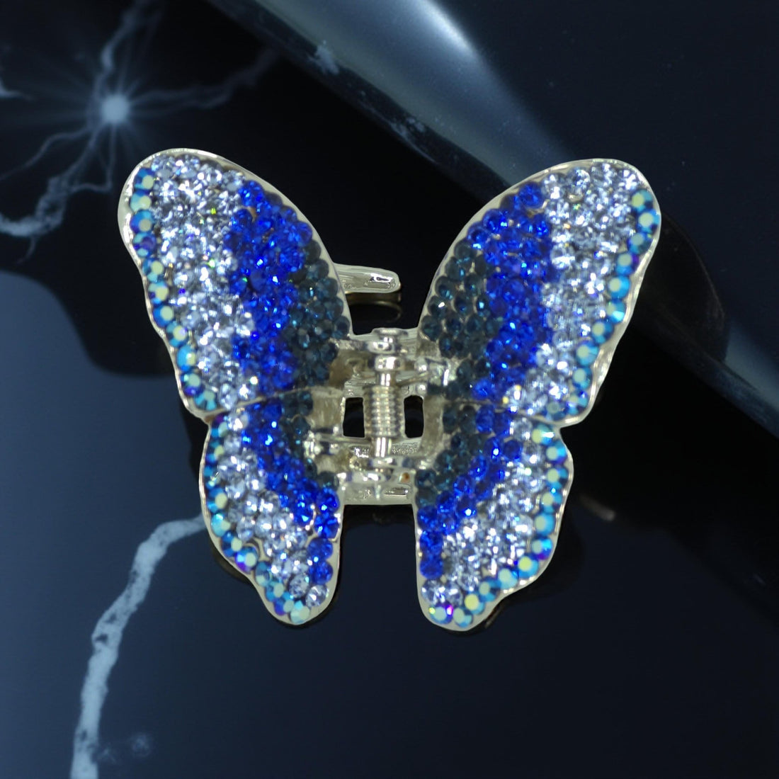 Haerime Papillora Mini Claw in Blue – sapphire butterfly clip placed on cream satin pouch with diffused natural lighting