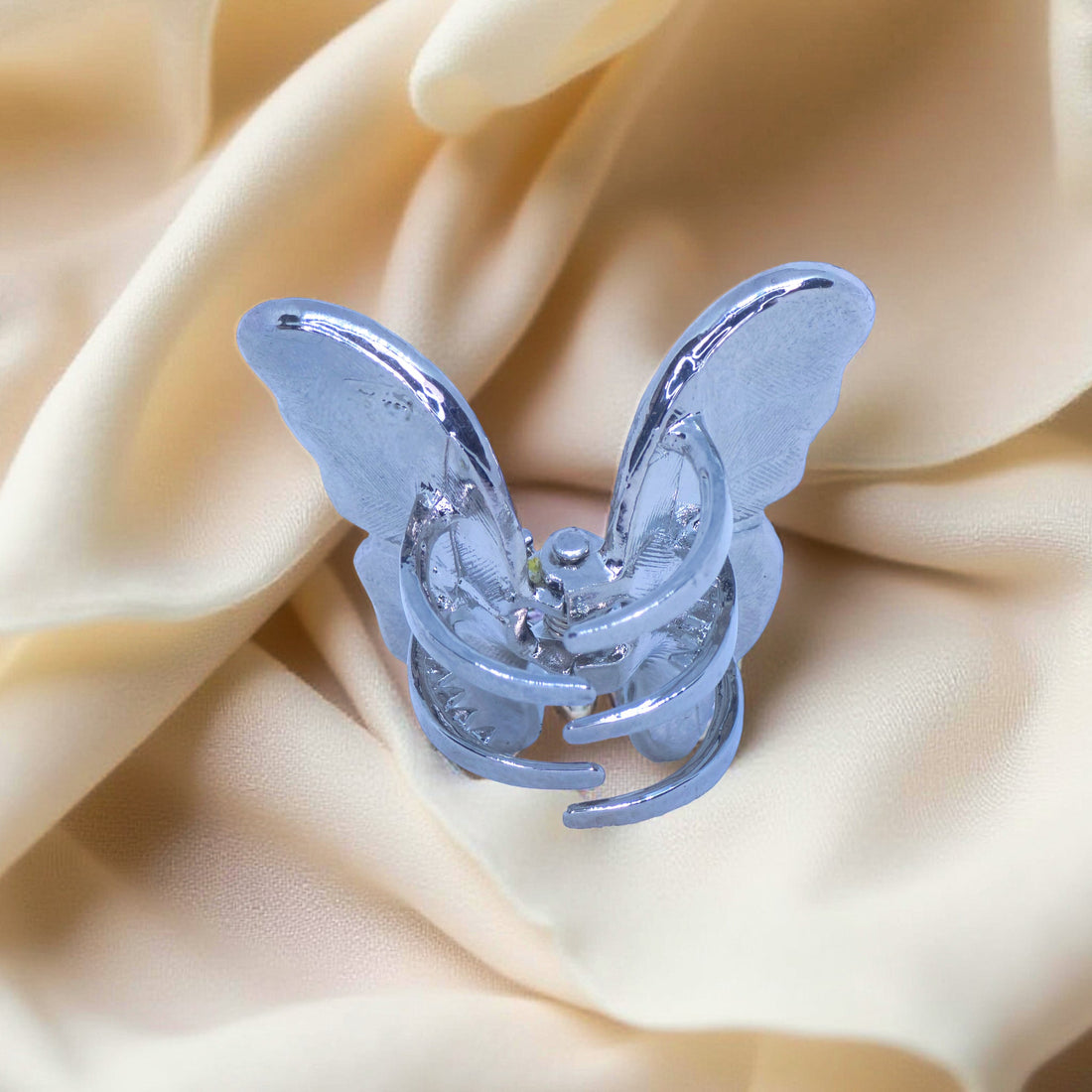 Haerime Papillora Mini Claw in Clear – rear angle showing magnetic claw base and silver-toned wings on creamy satin background