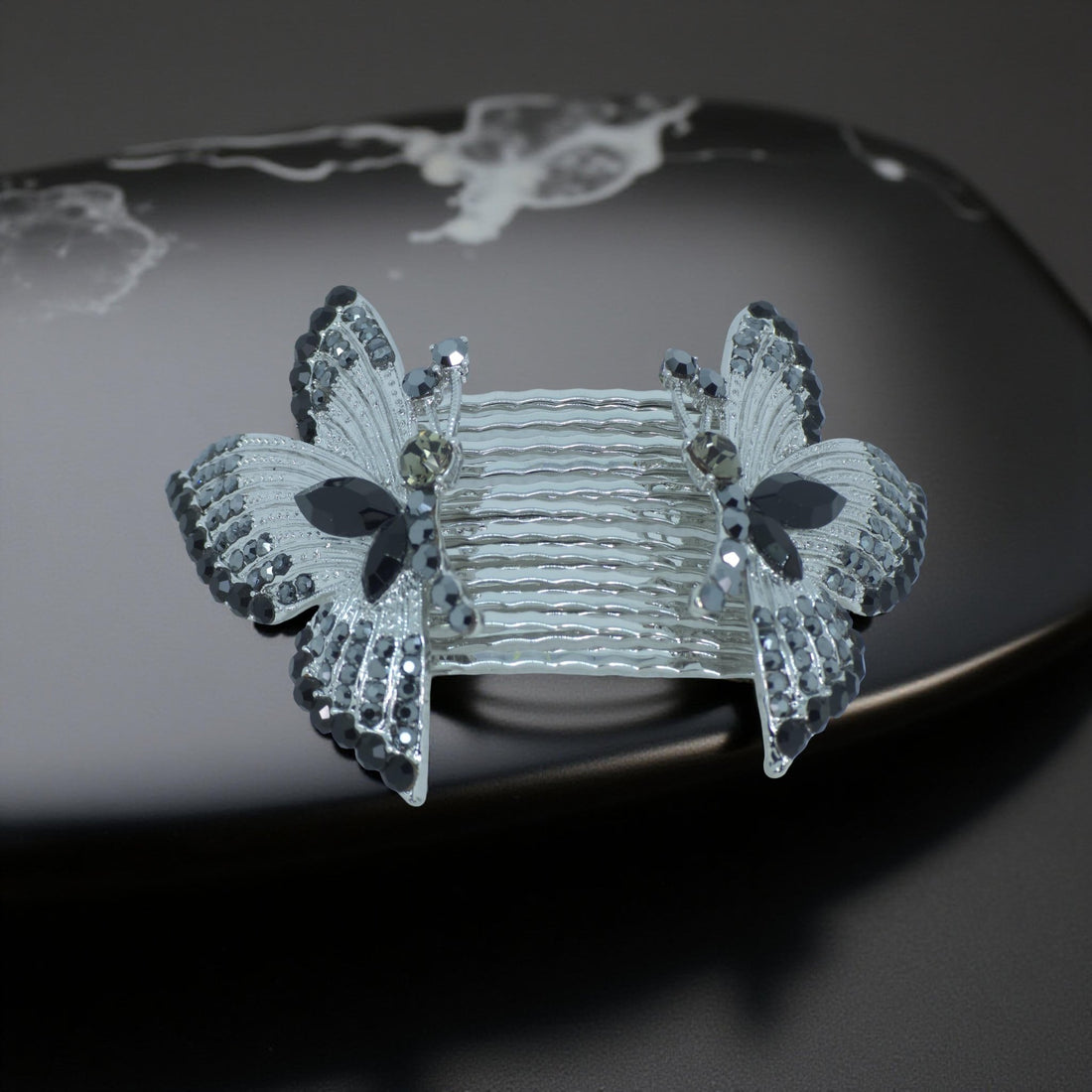 Haerime Papillora Twin Comb Set in Black – mirrored crystal wing combs resting on charcoal velvet with moody ambient glow