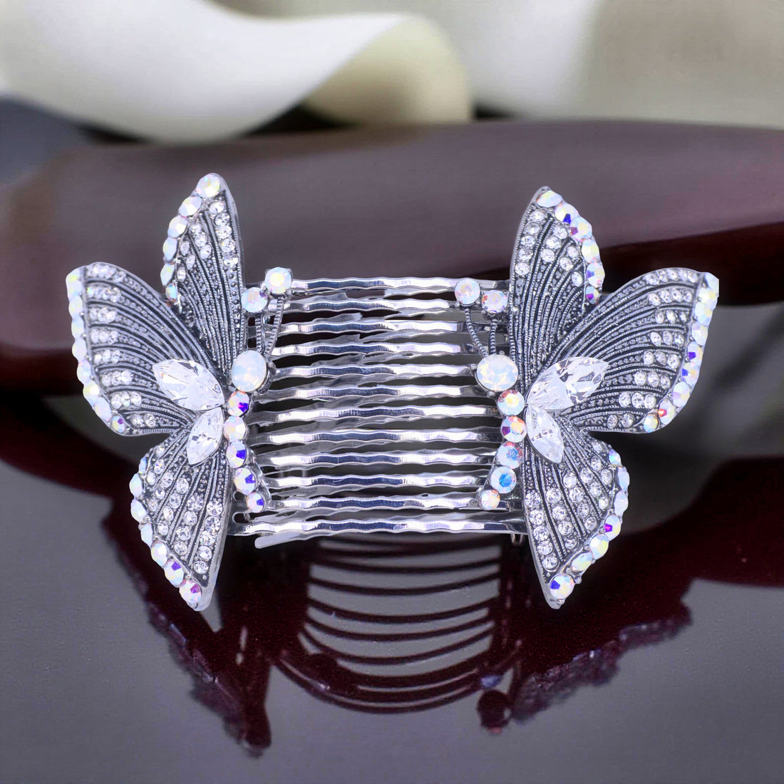 Haerime Papillora Twin Comb Set in Clear – mirrored crystal combs placed on soft ivory satin pouch with gentle daylight shadows