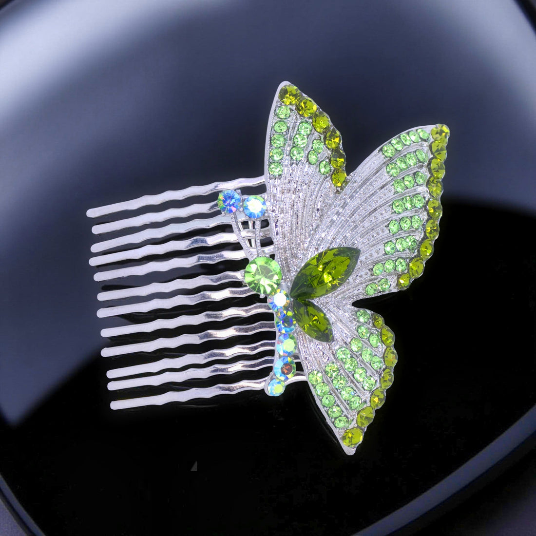 Haerime Papillora Twin Comb in Peridot – lime green crystal butterfly comb placed on glossy dark acrylic base under dramatic spotlight reflection