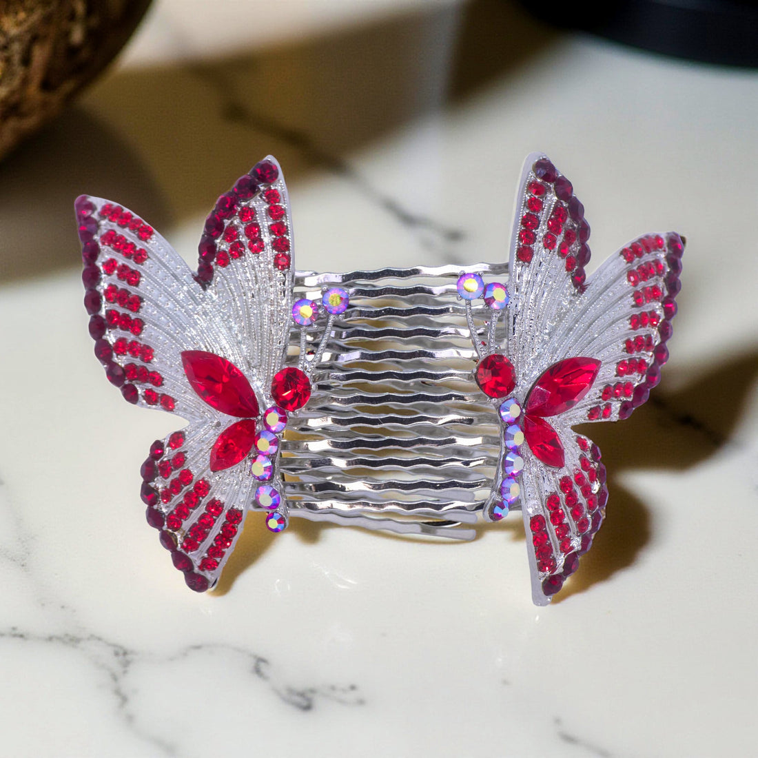 Haerime Papillora Twin Comb in Red – mirrored red butterfly wing combs placed on warm pink velvet with ambient lighting