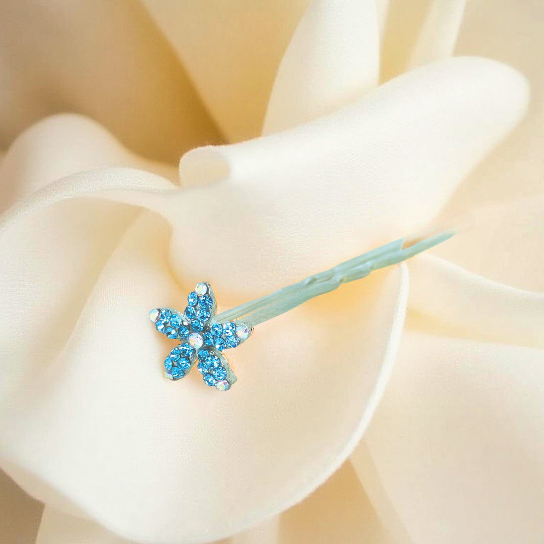 Haerime Petalight Hair Stick in Blue Zircon – crystal flower pin resting on ivory satin with soft reflection
