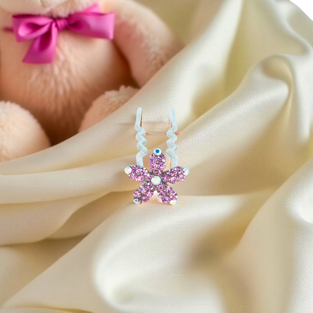 Haerime Petalight Hair Stick in Pink – five-petal pink flower clip placed on folded champagne satin in ambient lighting