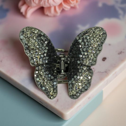 Haerime Papillora Mini Claw in Black – jet crystal butterfly jaw clip placed on matte pink ceramic tray with floral decor and soft ambient lighting