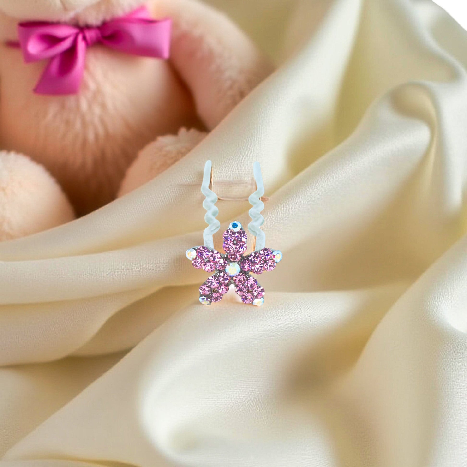 Haerime Petalight Hair Stick in Pink – five-petal pink flower clip placed on folded champagne satin in ambient lighting

