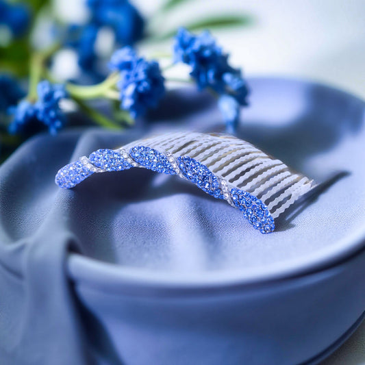 Haerime Seraphine Twist Comb in Blue – sculpted crystal ribbon comb displayed on lavender ceramic dish with blue blossoms in natural daylight
