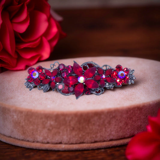 Haerime Serenbelle Bloom in Red – crystal floral barrette with ruby clusters displayed on beige velvet pedestal with red rose background
