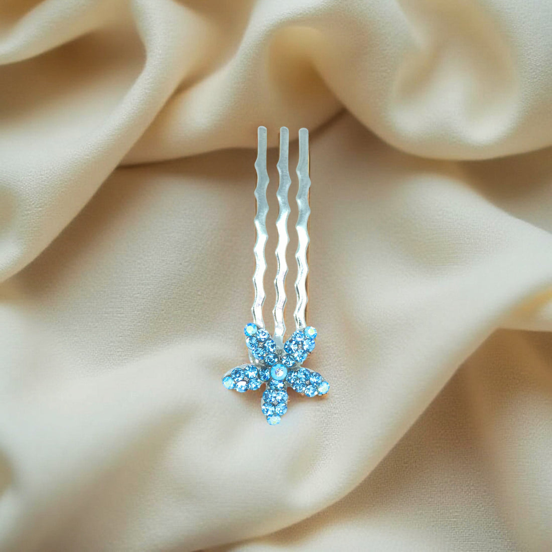 Haerime Starpetal Minis in Aquamarine – close-up of light blue pavé flower resting on silky blush fabric with subtle glow