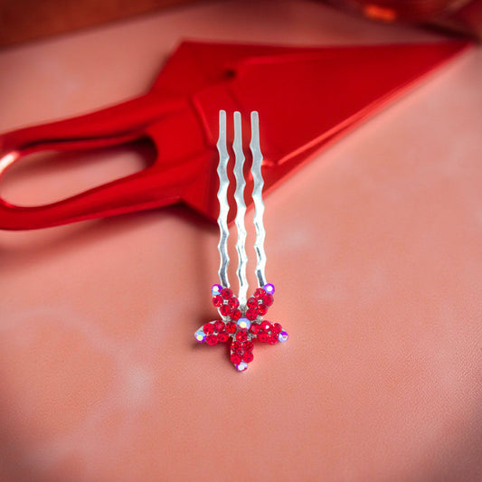 Haerime Starpetal Minis in Red – ruby crystal five-petal hair pin resting on peach satin tray with red scissors in vibrant spotlight
